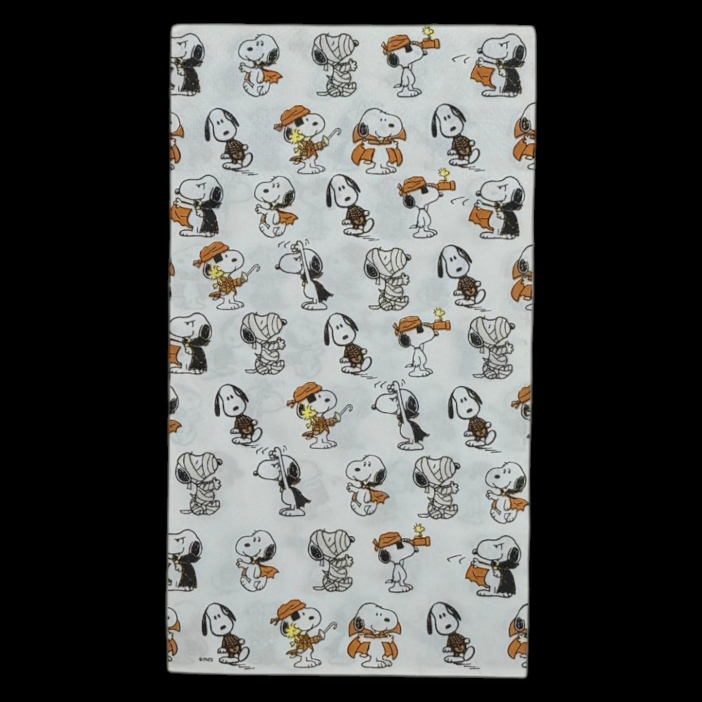 Guest-size decoupage paper napkin featuring an all-over tossed pattern of Snoopy and Woodstock in various Halloween costumes including vampire mummy and witch in classic Peanuts comic illustration style on a soft white background, photographed on a black surface.