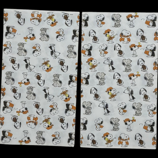 Guest-size decoupage paper napkin featuring an all-over tossed pattern of Snoopy and Woodstock in various Halloween costumes including vampire mummy and witch in classic Peanuts comic illustration style on a soft white background, photographed on a black surface.