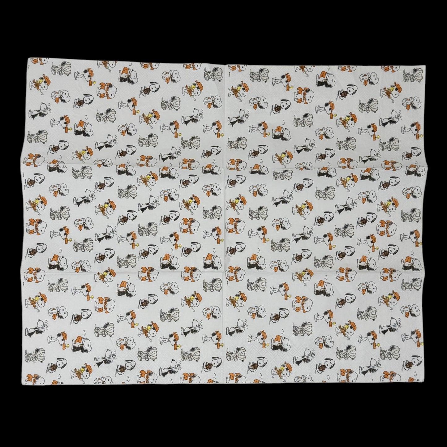 Guest-size decoupage paper napkin featuring an all-over tossed pattern of Snoopy and Woodstock in various Halloween costumes including vampire mummy and witch in classic Peanuts comic illustration style on a soft white background, photographed on a black surface.
