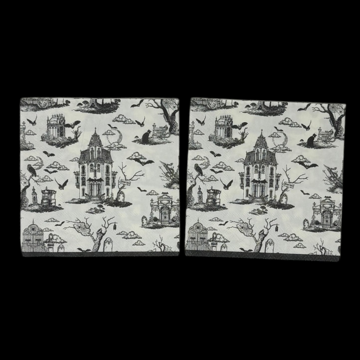Cocktail-size decoupage paper napkin featuring a richly detailed all-over Halloween toile print in black ink on soft cream white showing a Victorian haunted mansion flying bats crescent moon owl cemetery gates tombstones a black cat in a top hat gnarled dead trees and a zombie hand rising from the earth, photographed on a black surface.