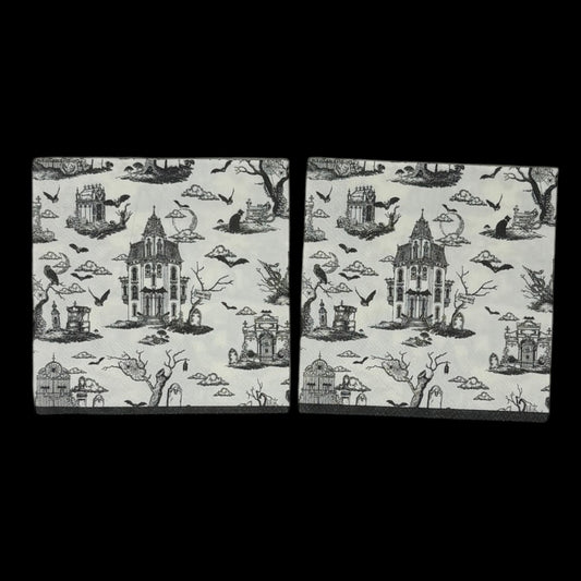 Cocktail-size decoupage paper napkin featuring a richly detailed all-over Halloween toile print in black ink on soft cream white showing a Victorian haunted mansion flying bats crescent moon owl cemetery gates tombstones a black cat in a top hat gnarled dead trees and a zombie hand rising from the earth, photographed on a black surface.