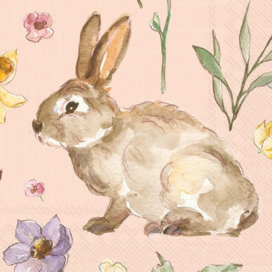 Close-up of two luncheon napkins featuring watercolor-style brown bunnies surrounded by pastel flowers and green leaves on a soft blush pink background.