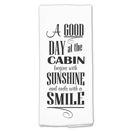 White towel with black text quote on a white background A good day at the cabin begins with sunshine and ends with a smile