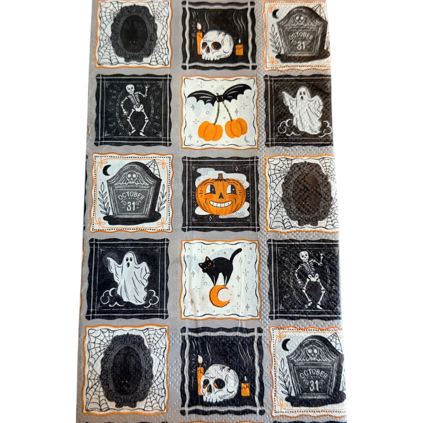 Guest-size decoupage paper napkin featuring a patchwork grid of fifteen individual framed Halloween icons including a skull with candles dancing skeleton friendly ghost grinning pumpkin black cat on crescent moon October 31 tombstone bat cherry and spider webs in black orange and white on a soft grey background