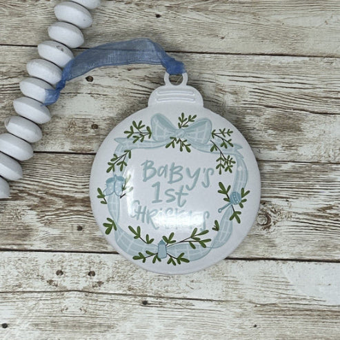 Decorative blue and white metal ornament with 'Baby's 1st Christmas' text on a wooden surface