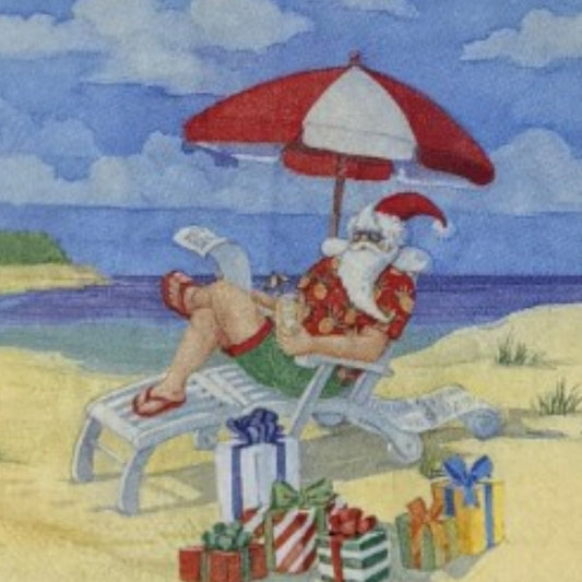 Cocktail-size decoupage paper napkin featuring an illustrated scene of Santa Claus relaxing in a beach lounge chair under a red and white striped umbrella wearing a Hawaiian shirt and flip flops with colorful wrapped gifts in the sand and a bright blue ocean in the background.