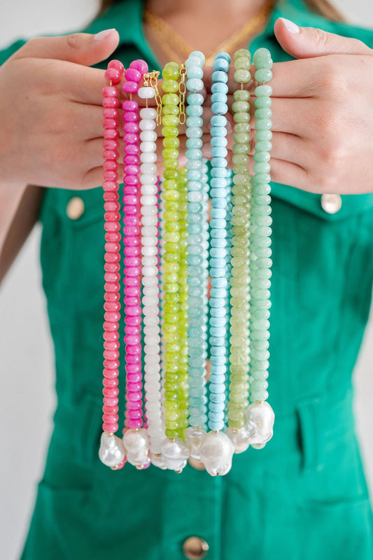 Person holding colorful beaded necklaces in front of a green shirt.