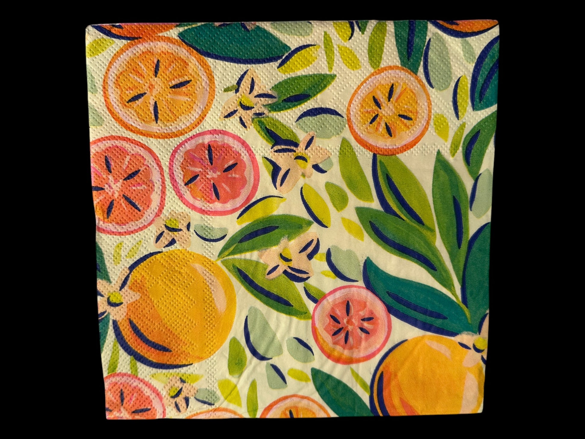 Close-up of a bright luncheon napkin featuring watercolor oranges, grapefruit, and green leaves designed by Kristen Vogel on a light cream background.